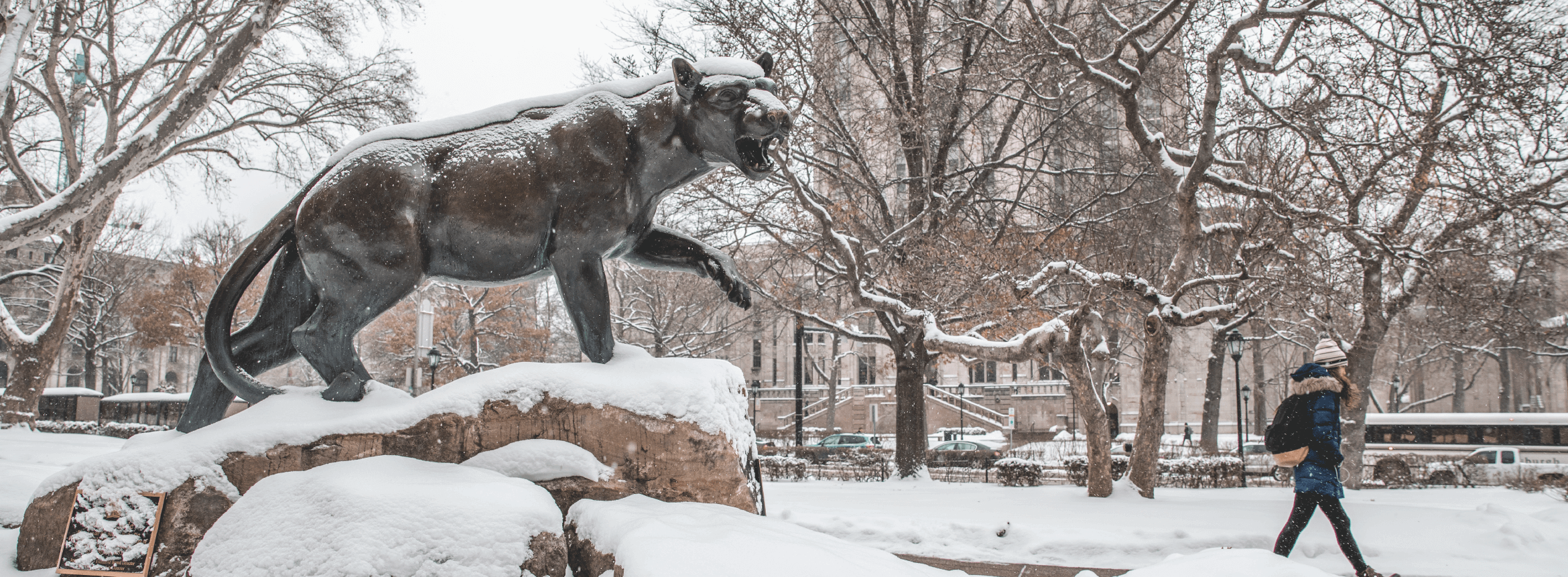 statue of pitt mascot covered in snow with pittsburgh campus in background