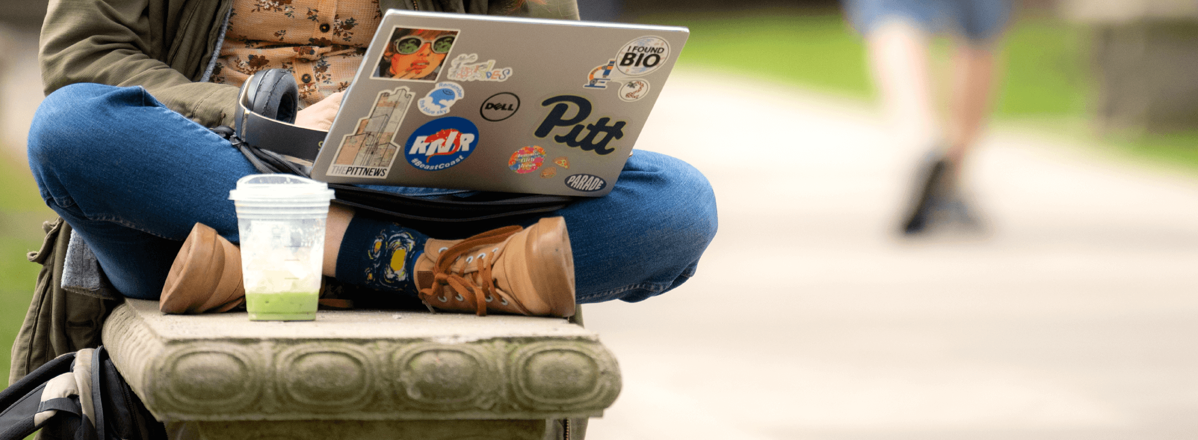 person sitting on a stone bench with a laptop in their lap
