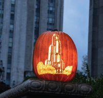 a pumpkin with the cathedral of learning carved into it. the pumpkin is lit from the inside.