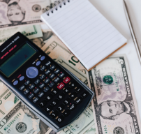 A calculator and notepad on top of some bills of various denominations